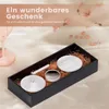 A gift set with cosmetic accessories laid out in a black box on a textured surface, with scattered flower petals in the background. Podgląd zdjęcia produktu