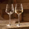 Two wine glasses, one empty and one filled with white wine, are placed on a wooden surface with a blurred background. Náhľad obrázku produktu