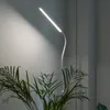 A white LED floor lamp with a curved neck is positioned next to a wall, with a large potted plant in the foreground. Anteprima dell’immagine prodotto