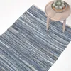 A blue striped rug is shown on a white background, with a small wooden side table and a potted cactus to the right. Náhled obrázku produktu