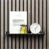 A black shelf mounted on a slatted wall, displaying a book, a bottle of yellow liquid, and a white clock. Produktbild-Vorschau