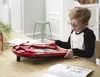 A young boy is playing with a red toy on a wooden table. Produktbild-Vorschau