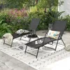 Two black lounge chairs are set up on a patio with a rug and plants in the background. Náhled obrázku produktu