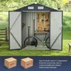 An open metal shed in a garden setting, filled with gardening tools and a bicycle. Two cardboard boxes are shown in the foreground. Náhled obrázku produktu