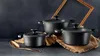 Three black pots of different sizes are arranged on a burlap cloth, with a golden frame in the background and a golden spoon in the foreground. Produktbild-Vorschau