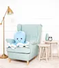 A blue plush octopus sits on a light blue armchair next to two small side tables, one with a vase and alarm clock. A gold floor lamp is to the left. Anteprima dell’immagine prodotto