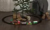 A Christmas train set is arranged around the base of a Christmas tree, with gifts and slippers nearby. Podgląd zdjęcia produktu