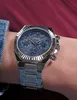A close-up shot of a silver Guess watch with a blue face on a person's wrist. Voir les images du produit