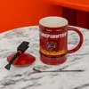 A firefighter-themed mug with its lid and a spoon on a marble table. Produktbild-Vorschau