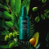 A bottle of Aveda Botanical Repair Strengthening Overnight Serum is placed among lush green leaves and avocados, with some green berries on a branch. Anteprima dell’immagine prodotto