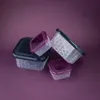 A set of four clear plastic food storage containers with patterned sides and colored lids, arranged on a purple background. Produktbild-Vorschau