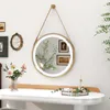 A round mirror with LED lights is hanging on a wall above a white vanity table. There are flowers in a vase on the table, and some decorative items. Anteprima dell’immagine prodotto