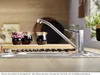 A kitchen sink area with a faucet, jars of jam, and a wooden board. Produktbild-Vorschau