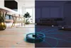 A robot vacuum cleaner is shown in a split image, with one half depicting a modern living room in daylight and the other half showing a living room at night, with blue lines indicating the robot's cleaning path. Produktbild-Vorschau