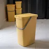 Several yellow plastic trash cans with lids and handles are arranged in a room with tiled flooring. Produktbild-Vorschau