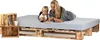 A woman and a child are lying on a bed frame made of wooden pallets, with a mattress on top. There are wooden crates next to the bed. Produktbild-Vorschau