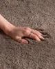A hand with rings is pressing into a soft, shaggy brown carpet. Náhled obrázku produktu