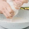 Hands squeezing a white cloth into a bowl of white liquid. Produktbild-Vorschau