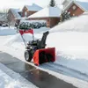 A snow blower is clearing snow from a driveway in a suburban neighborhood during winter. Produktbild-Vorschau