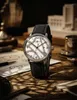 A watch is placed on a wooden table with papers and other objects around it. Voir les images du produit