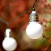 A close-up shot of two white globe-shaped lights on a string, with a blurred background of red and green foliage. Náhľad obrázku produktu