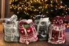 Four Christmas-themed drawstring bags are arranged in front of a blurred Christmas tree with lights. Anteprima dell’immagine prodotto