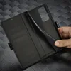 A hand is holding open a black leather wallet-style phone case, revealing the interior card slots and the phone holder. Produktbild-Vorschau