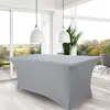 A rectangular table covered with a light gray, form-fitting tablecloth is shown in a well-lit room with large windows overlooking a natural landscape. Two white pendant lights hang above the table. Produktbild-Vorschau
