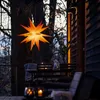 An illuminated star lantern hangs from a tree next to a wooden cabin and outdoor seating area. Produktbild-Vorschau