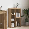 A wooden bookshelf with items on its shelves, next to a desk and a large plant. Náhľad obrázku produktu