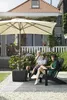 A family relaxing on a patio under an umbrella with a house in the background. Produktbild-Vorschau
