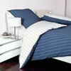 A neatly made bed with blue and white striped bedding, a bedside table with a lamp and decorative balls. Produktbild-Vorschau