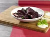 A bowl of sliced beets with herbs, served on a wooden cutting board with bread and cheese. Produktbild-Vorschau