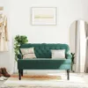 A dark green velvet bench with tufted backrest and two pillows is placed in a room with a coat rack, a plant, a framed picture, and a large arched mirror. Náhled obrázku produktu