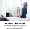 A woman stretching on a bed next to a black air cooler in a bright room. Produktbild-Vorschau