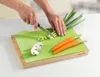 A person is chopping green onions on a cutting board with a knife. There are also mushrooms and carrots on the cutting board. Anteprima dell’immagine prodotto