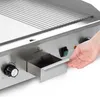 A close-up shot of a person's hand reaching for a drawer on a grill. Náhled obrázku produktu