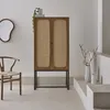 A wooden cabinet with rattan doors stands in a minimalist room with a chair and decorative items. Produktbild-Vorschau