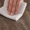 A hand is wiping a wooden surface with a white cloth, showing water droplets on the surface. Anteprima dell’immagine prodotto