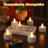 A set of LED tea lights with a charging base and remote control, arranged on a table with a glass of wine and flowers in the background. Produktbild-Vorschau