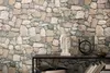 A stone-effect wallpaper is shown as a backdrop for a shelf with decorative items. Produktbild-Vorschau