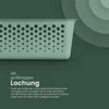 A close-up of a green storage basket with a perforated design, set against a dark green background with concentric circles. Voir les images du produit