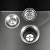 A close-up view of sink drain components, including a stopper, a strainer basket, and the drain opening itself, set against a dark background and a metallic sink surface. Podgląd zdjęcia produktu