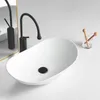 A white oval countertop sink with a black faucet and drain. Náhľad obrázku produktu