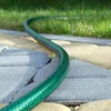 A green garden hose lies on a paved pathway next to a lawn. Anteprima dell’immagine prodotto