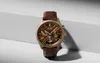 A men's chronograph watch with a brown leather strap and a brown dial, placed on a light gray and white surface. Anteprima dell’immagine prodotto