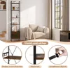 A tall, narrow bookshelf with a rustic brown finish and black metal frame is shown in a room with a beige armchair and a window. Produktbild-Vorschau