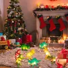 A Christmas tree and fireplace decorated for the holidays, with illuminated dinosaur-shaped string lights on the floor. Produktbild-Vorschau