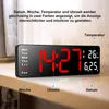 A digital clock displayed on a shelf, with text overlays and labels pointing to different features. Produktbild-Vorschau