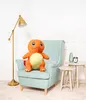 A plush toy Charmander sits on a chair in a room with a floor lamp and side tables. Voir les images du produit